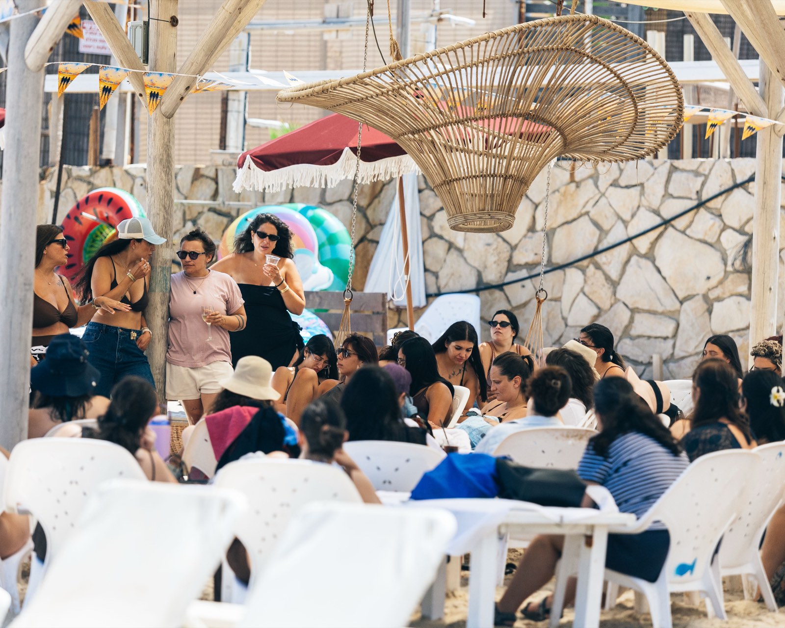 Dozens of women sitting together under a pergola at a seaside community event