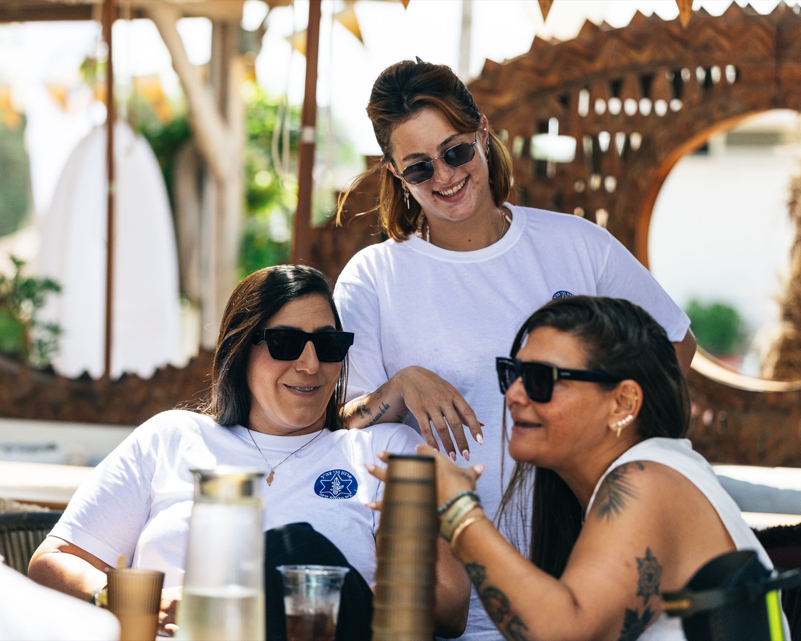 Three women in IDF Disabled Veterans Organization shirts laughing together at a beach gathering